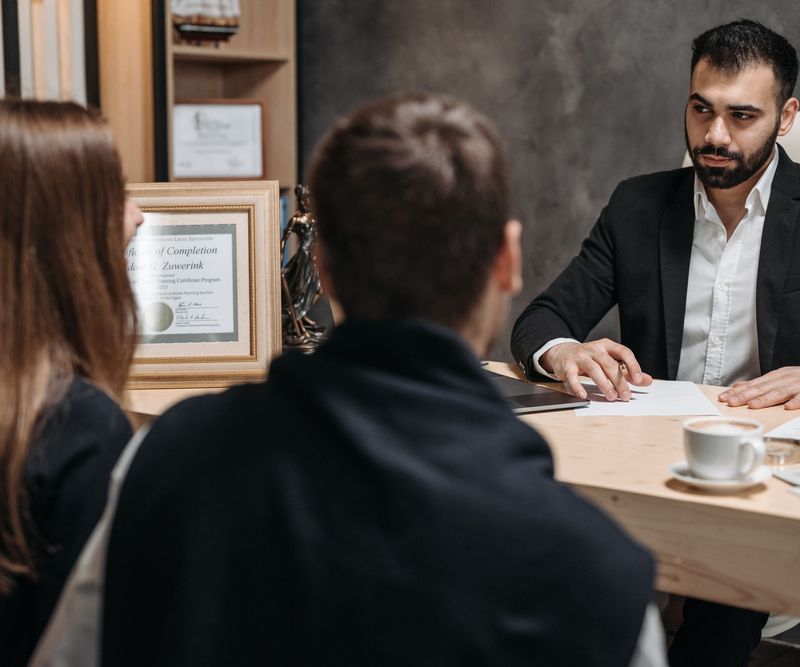 A finance professional discussing loan options with two customers across a desk in a modern office