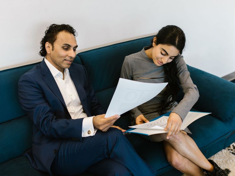 Two people reviewing loan documents together on a sofa in an office